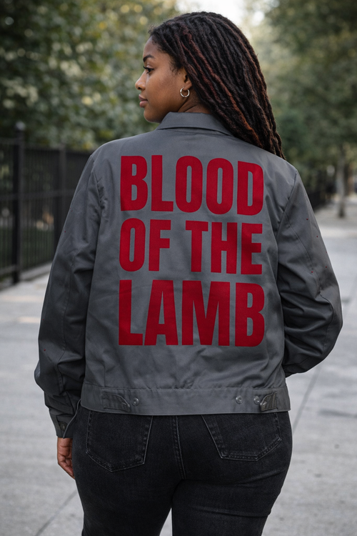 Person wearing a jacket with 'Blood of the Lamb' text outdoors